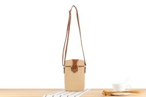 Close-up of paper rope woven cylinder bag with brown leather lid and gold twist lock