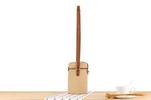 Close-up of woven paper rope texture and brown leather strap on cylindrical bag