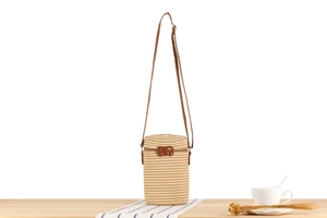 Detail of a beige woven cylindrical crossbody bag with brown leather zipper and slim strap