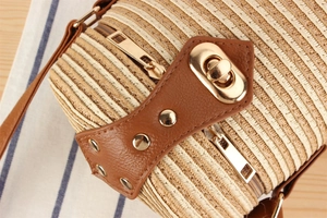 Detail of paper rope woven cylinder bag featuring brown leather trim and golden hardware