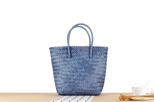 Blue hand-woven plastic tote bag on wooden table with elegant lifestyle props