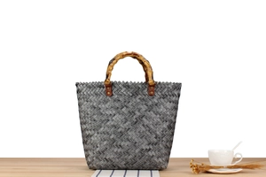 Detail of grey woven tote bag with natural bamboo handle and vintage leather accents