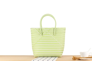 Detail of woven plastic beach bag showing green and white herringbone texture and handle