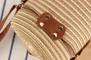 Detail of cylindrical woven paper bag with brown leather patch and gold studs