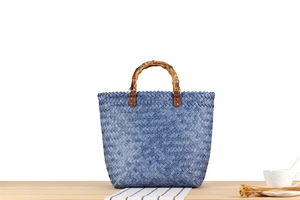 Detailed close-up of blue woven summer bag featuring retro bamboo handles and gold rivets