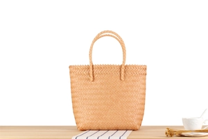 Detail view of a woven plastic tote bag with sturdy top handles on a wooden table