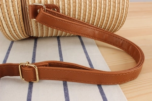 Close-up detail of paper rope cylinder bag with brown leather strap and gold buckle