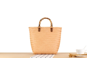 Detail of woven straw tote bag featuring a natural bamboo handle and leather fasteners