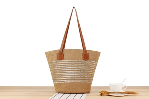 Detailed close-up of woven straw tote bag with silver stripes on a wooden table
