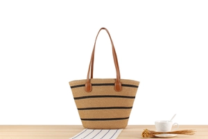 Detail of hand-woven striped straw tote bag with leather handles on a wooden table