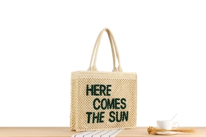 Detailed view of beige woven tote bag with green embroidered sun slogan on wooden table