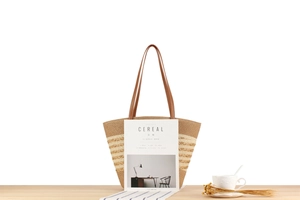 Detail of hand-woven striped straw tote bag with brown leather handles on wooden table