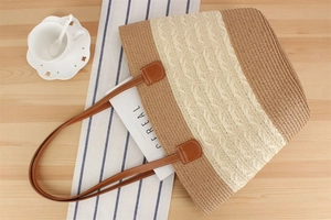 Detail of hand-woven striped straw tote bag with brown leather handles on wooden surface