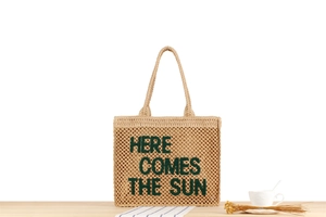 Detail of embroidered 'HERE COMES THE SUN' text on beige woven straw tote bag