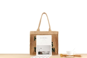 Macro detail of beige woven tote bag showing green embroidered letters and mesh texture