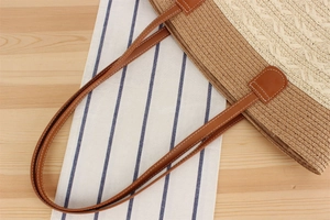 Detail of hand-woven straw tote with brown leather strap and white stitching
