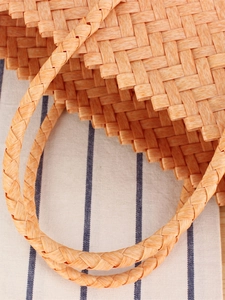 Handcrafted orange woven tote bag with round handles on blue and white linen background