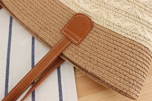 Close-up of woven straw tote bag detailing bi-color stitching and faux leather strap