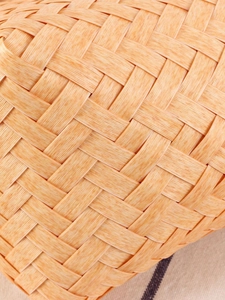 Handwoven rattan-style handbag with detailed twill weave on warm beige textile background
