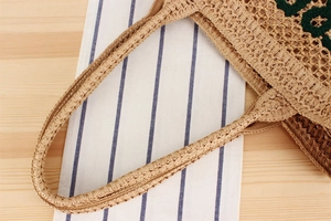 Close-up of hand-woven straw bag featuring green embroidered letters and natural texture