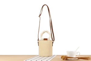 Detail of woven straw bucket bag featuring a white beaded handle and brown leather strap