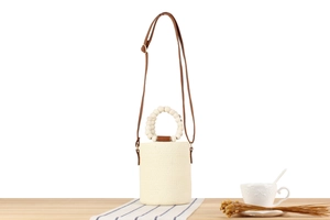 Detail of paper rope woven bucket bag with white bead handle and brown leather straps