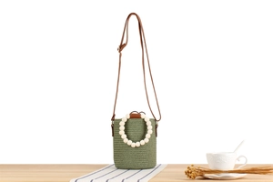 Detail of sage green woven bucket bag featuring a white beaded handle and leather strap