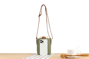 Mini green woven straw bucket bag with pearl trim and leather strap next to phone