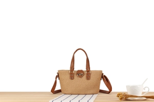 Detail of woven straw tote bag featuring brown leather trim and golden twist lock