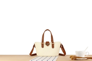 Close-up of woven straw handbag with brown leather strap and gold metallic lock detail
