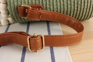 Detail of green woven straw bag featuring brown leather strap and gold buckle