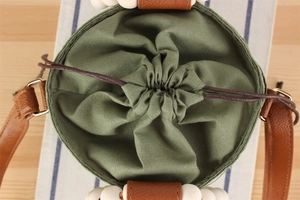 Detail of green woven bag featuring brown drawstring closure and decorative white wooden beads