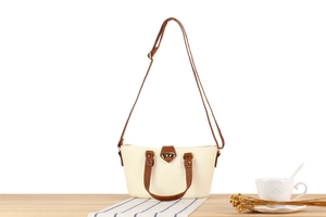 Detailed view of woven straw tote bag with brown leather straps and metal twist lock