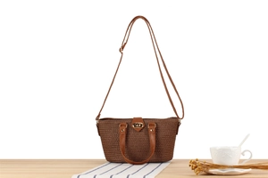Close-up of brown woven shoulder bag with golden metal twist lock on a wooden table