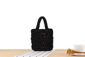 Detail of black hand-woven tote bag with hollow mesh texture on a wooden table