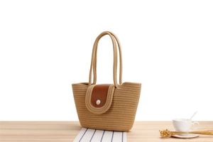 Detailed macro view of khaki woven straw bag with dark brown leather flap and pearl detail