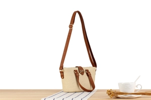 Detailed view of woven straw handbag with brown leather straps and gold buckle