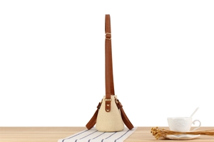 Close-up of beige woven bucket bag with brown leather strap and gold buckle detail