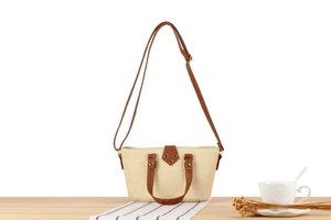 Detail of cream woven tote bag featuring brown leather handles and adjustable shoulder strap