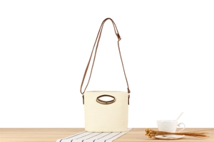 Detail of cream woven bucket bag with oval gold handle on light wooden table