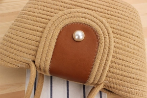 Detail view of woven straw bag with brown leather flap and large pearl button closure