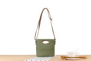 Detail of light green woven crossbody bag with metal handle and brown leather strap