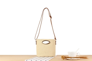 Detail of beige paper rope woven crossbody bag with gold metal handle and leather strap