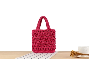 Detail of handmade hollow woven handbag in rose red with crochet texture on a wooden desk