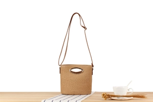 Detail of woven straw bucket bag with oval metal handle and slim brown leather strap