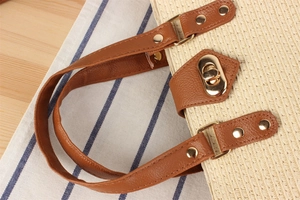 Detail of woven straw handbag with brown leather handles and golden metal twist lock