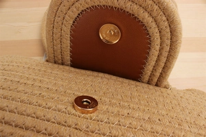 Detail of the magnetic buckle closure on a straw woven bag with brown leather trim