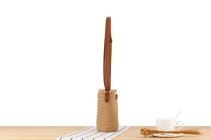 Close-up of beige woven paper rope bucket bag with brown leather strap and metal rivets