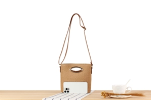 Detail of hand-woven paper rope bag with elegant gold metal handle on a wooden table