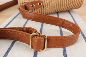 Detail of adjustable brown PU leather strap with gold buckle on woven straw crossbody bag